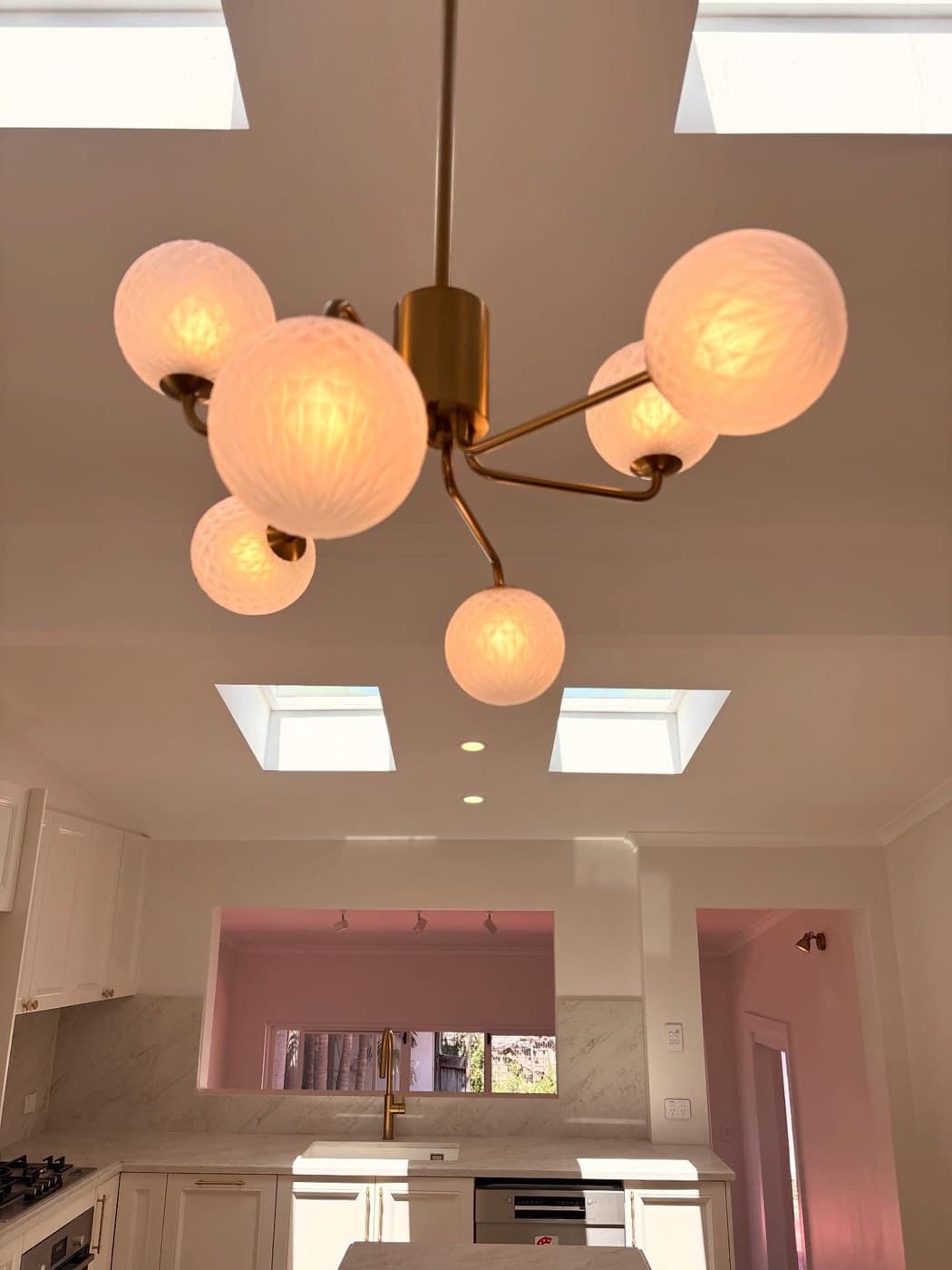 A brass chandelier with frosted globes under a skylight