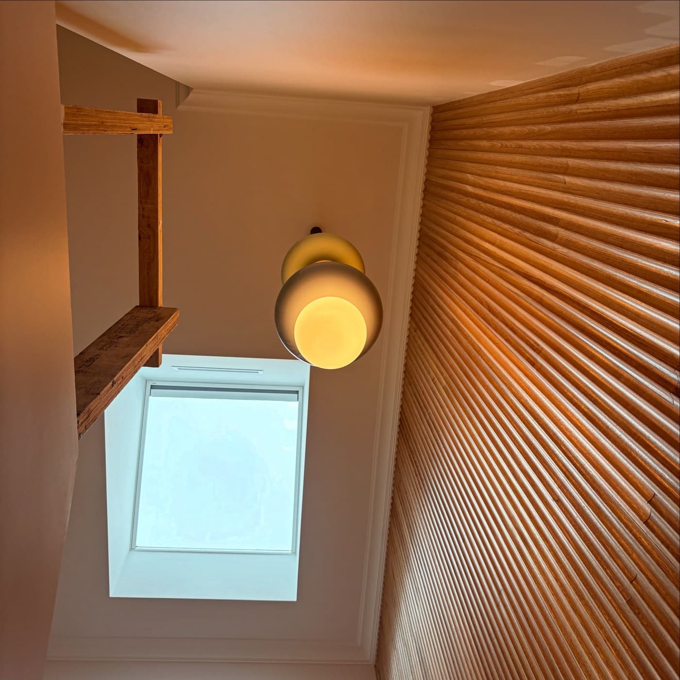 A globe pendant under a skylight beside a timber batten wall