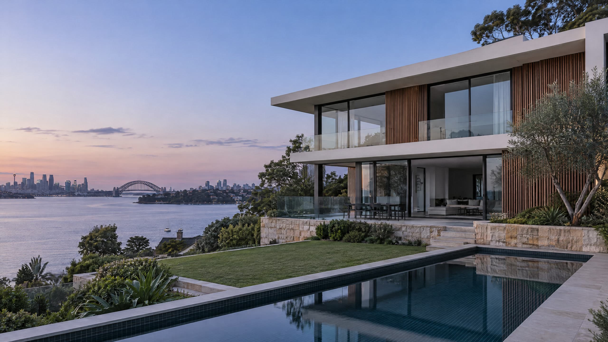 A contemporary waterfront home on Sydney's Lower North Shore at dusk, with the Harbour Bridge and city across the water